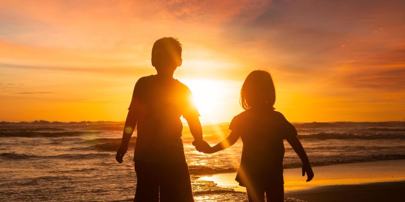 two kids on a beach with their guardian at sunset
