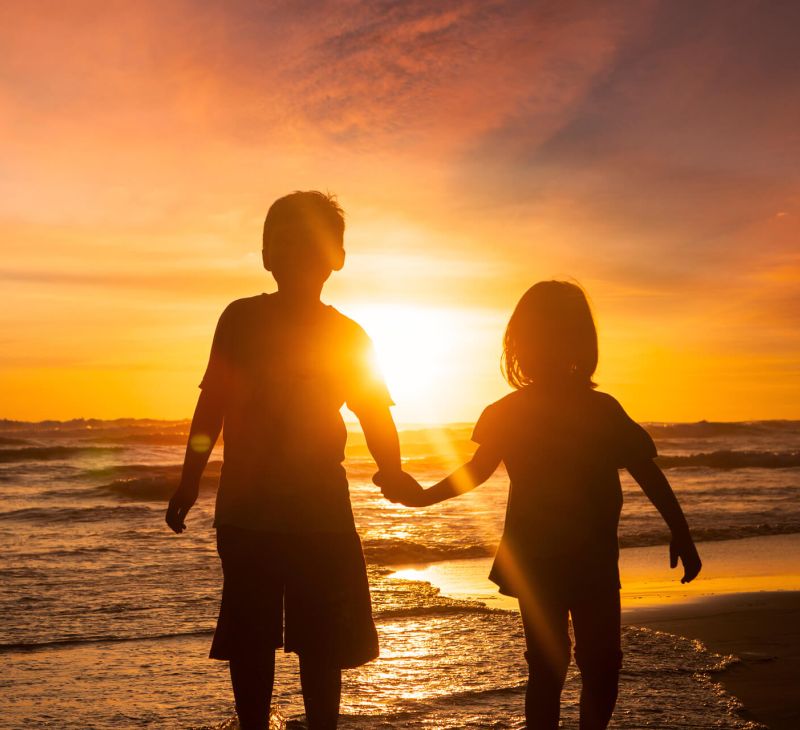 two kids on a beach with their guardian at sunset
