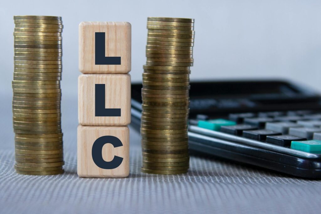 Should You Use an LLC for Estate Planning - Virginia Beach Law Group Wooden blocks labeled "LLC" stand between two stacks of coins, while a calculator rests in the background, suggesting a financial or business context focused on limited liability companies.